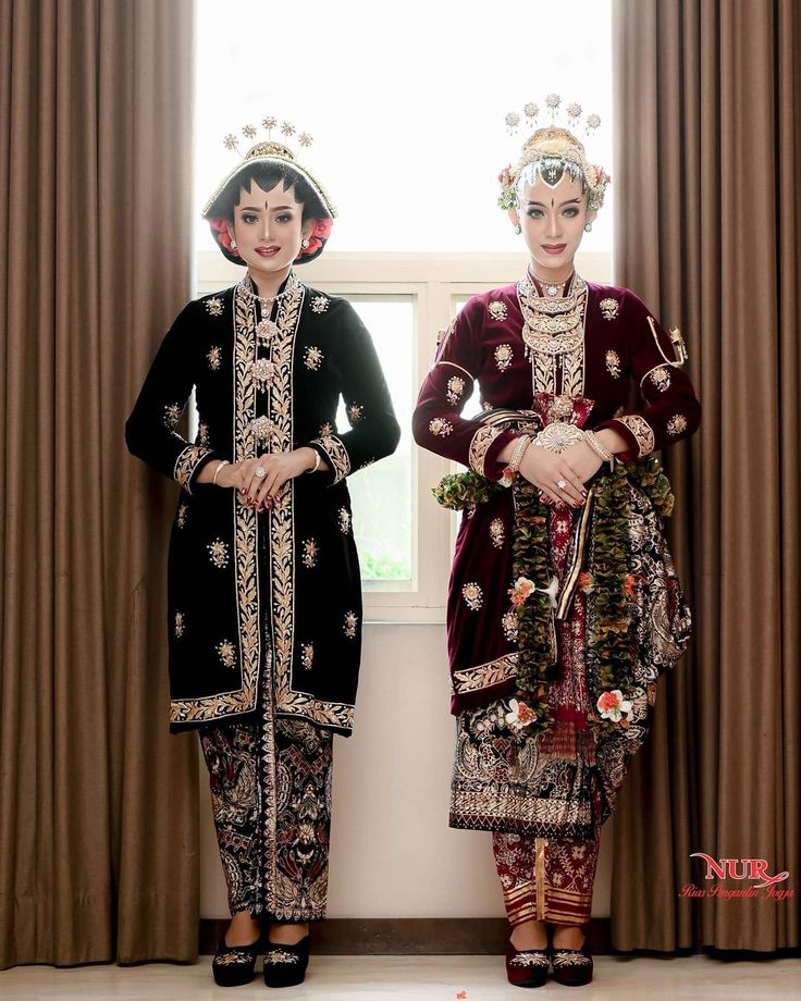 two women standing next to each other in front of a window wearing ethnic clothing and headpieces