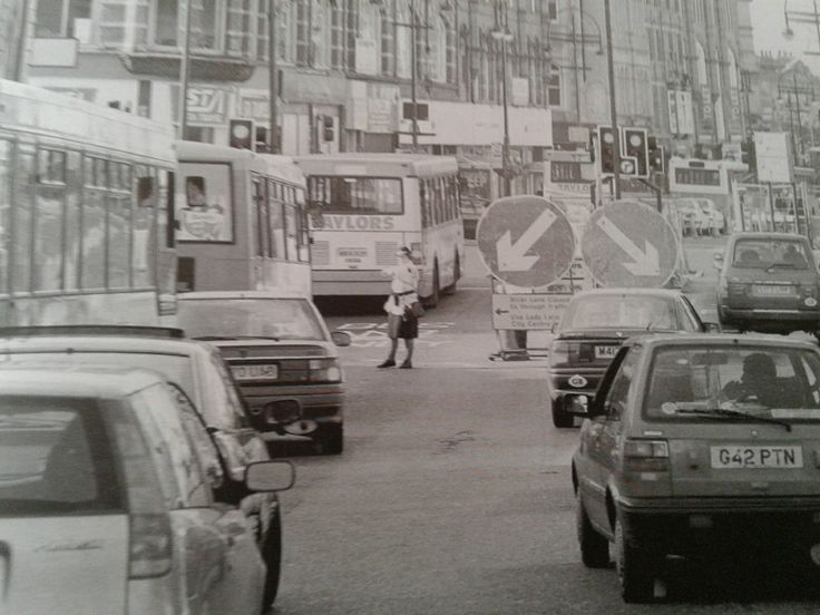 black and white photograph of traffic on a city street with buses, cars and people