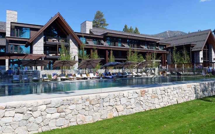 an outdoor swimming pool with chaise lounges and umbrellas in front of a large building