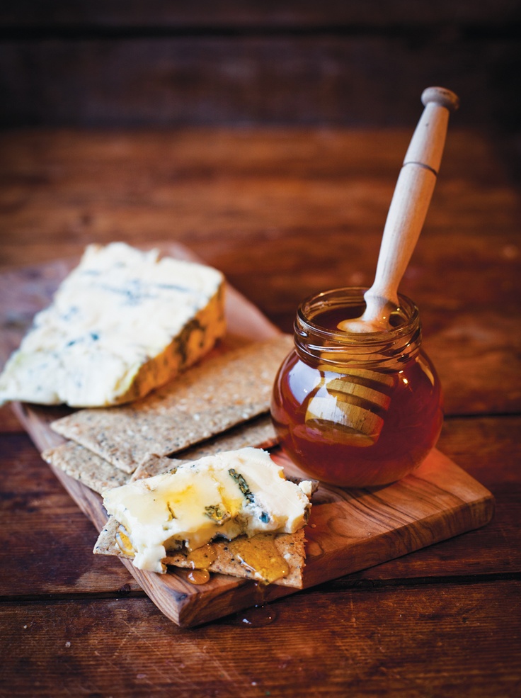 a wooden cutting board topped with cheese and crackers next to a jar of honey