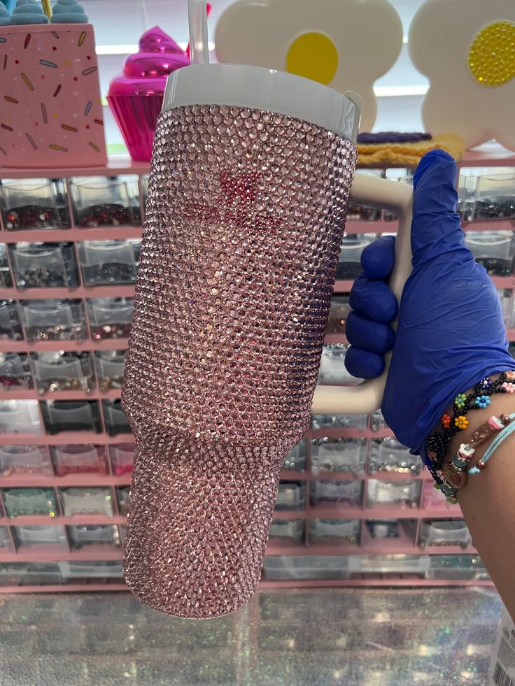 a person wearing blue gloves holding up a pink cup in front of a store display