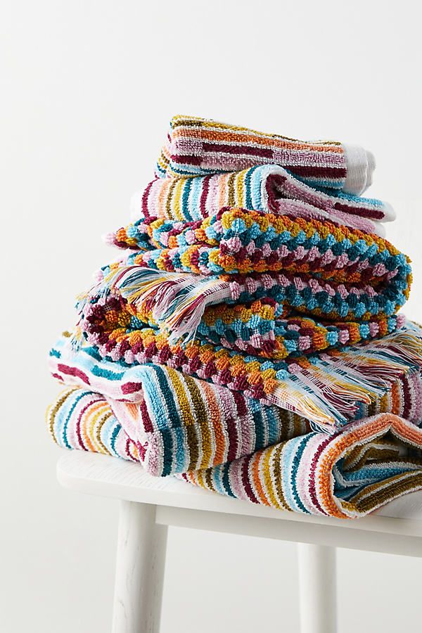 stack of multicolored towels sitting on top of a white stool