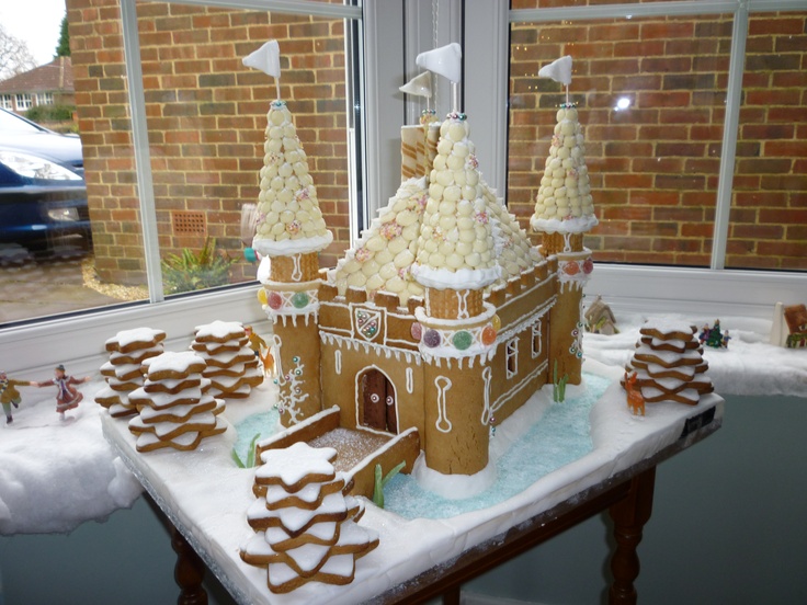 a gingerbread castle is on a table in front of a window with snow and icing