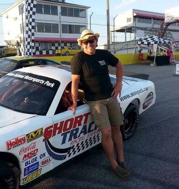 a man sitting on the hood of a racing car in front of a race track