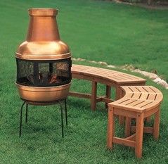 a wooden bench sitting in the grass next to an outdoor fire pit on top of a field