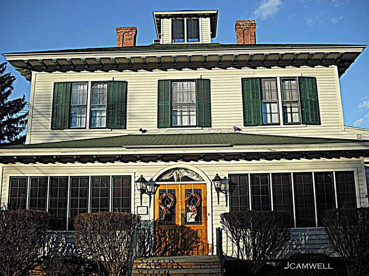 a large white house with green shutters and a clock on the front door is shown