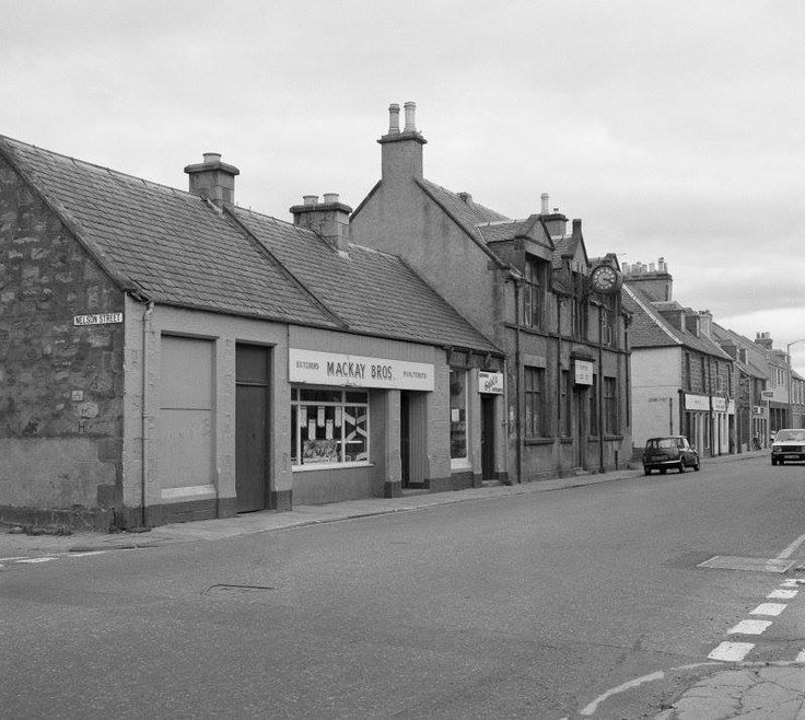 a black and white photo of an old town street with cars parked on the side