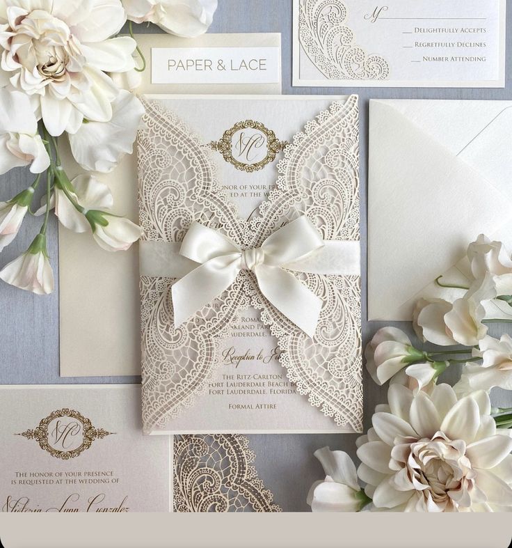 the wedding stationery is laid out with white flowers and lace on it's side