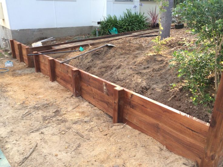 a wooden garden bed in the middle of a yard with dirt on the ground and trees