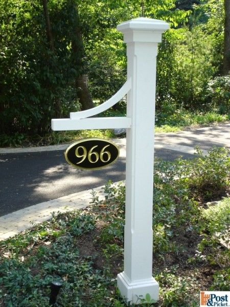 a white mailbox with a black address sign in front of some bushes and trees