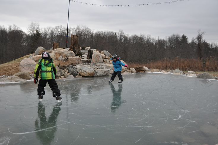 two people skating on an ice rink with rocks and trees in the backgroud