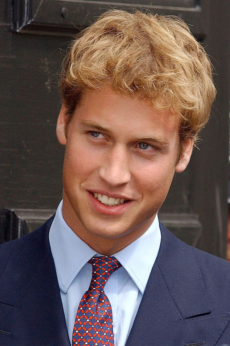 a young man with blonde hair wearing a suit and tie smiling at the camera while standing in front of a door