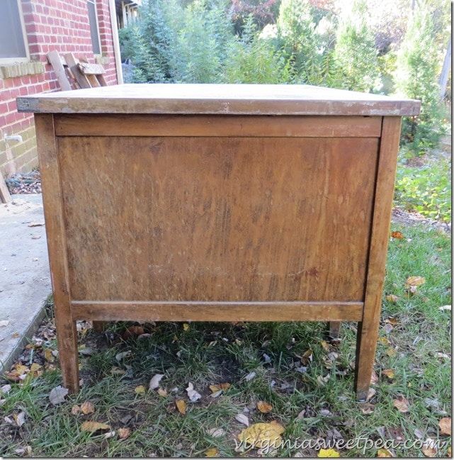 an old wooden chest sitting in the grass next to a brick building with trees and bushes behind it