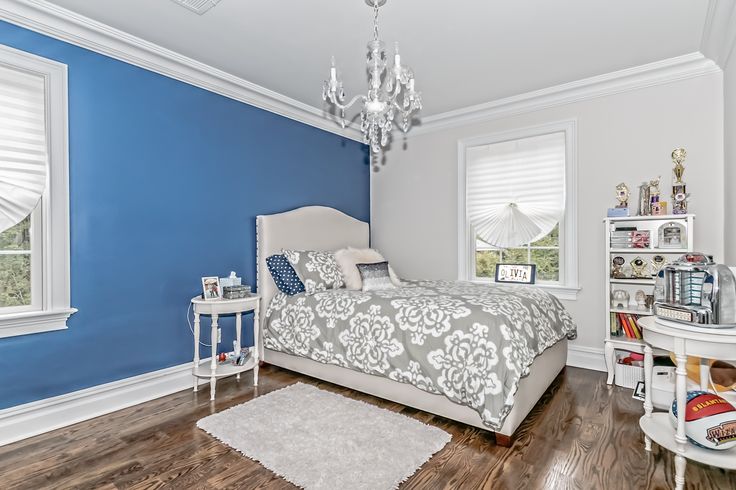 a bedroom with blue walls and hardwood floors, white furniture and a chandelier hanging from the ceiling