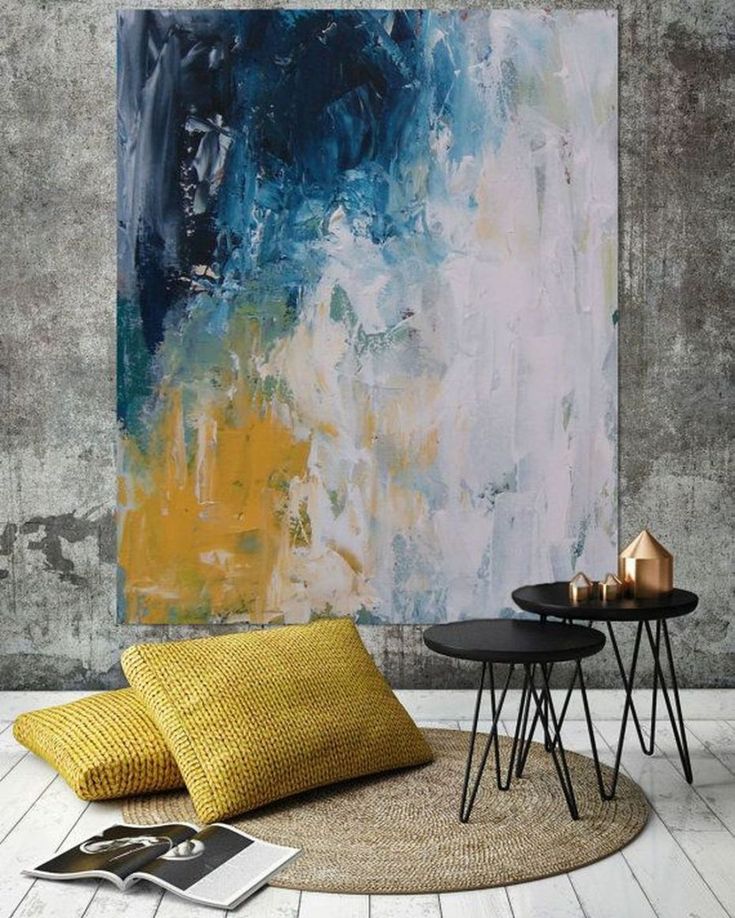 an abstract painting hangs on the wall next to two small tables with yellow and blue pillows