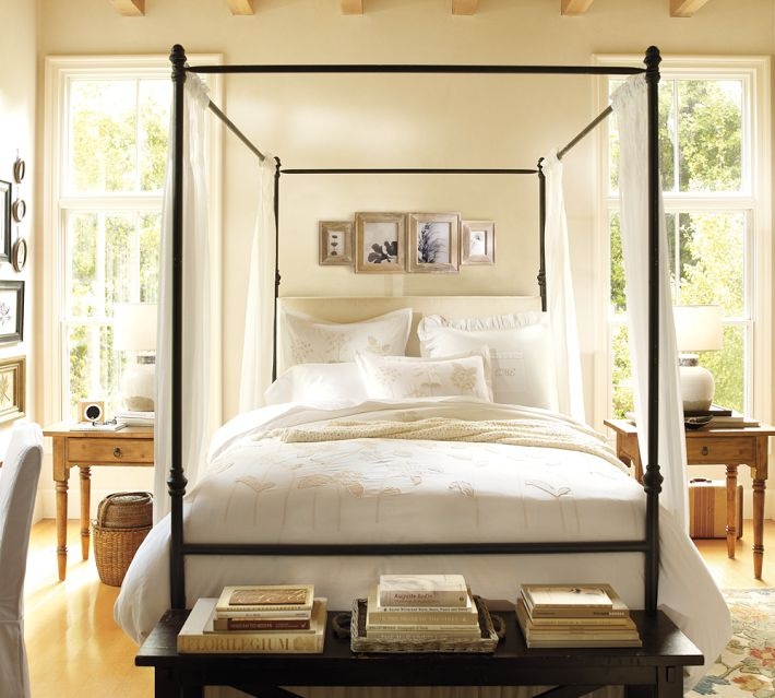 a four poster bed with white sheets and pillows in a bedroom next to two windows