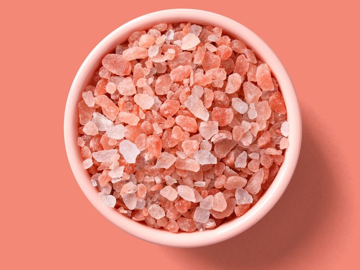 a pink bowl filled with small rocks on top of a pink surface, next to an orange background