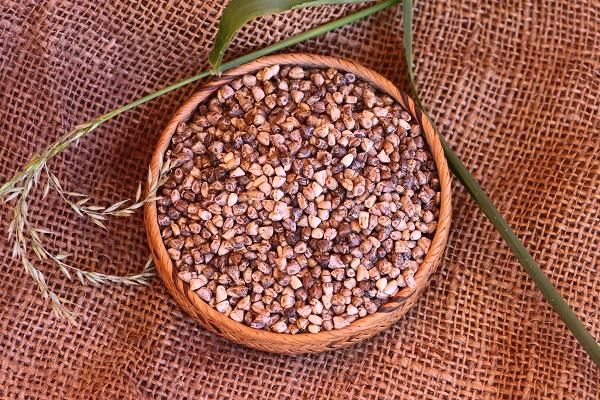 a wooden bowl filled with seeds on top of a brown cloth next to a green plant