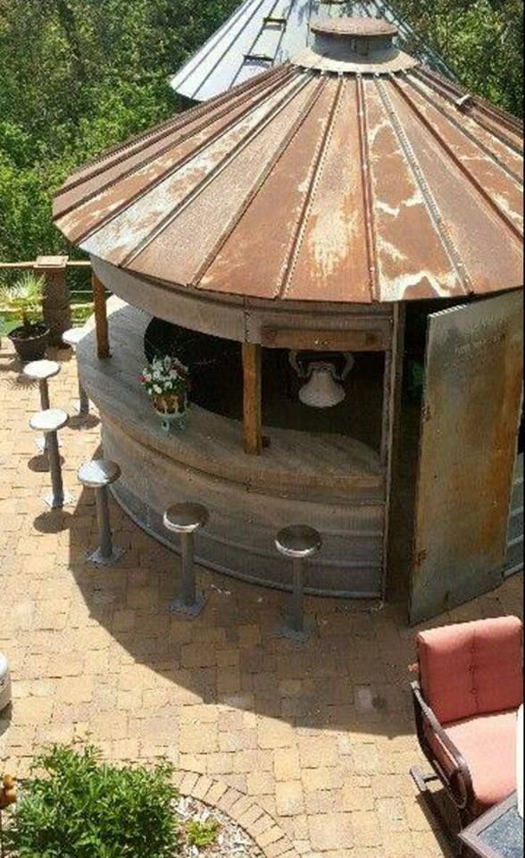 an outdoor kitchen made out of a round metal structure with stools and tables around it