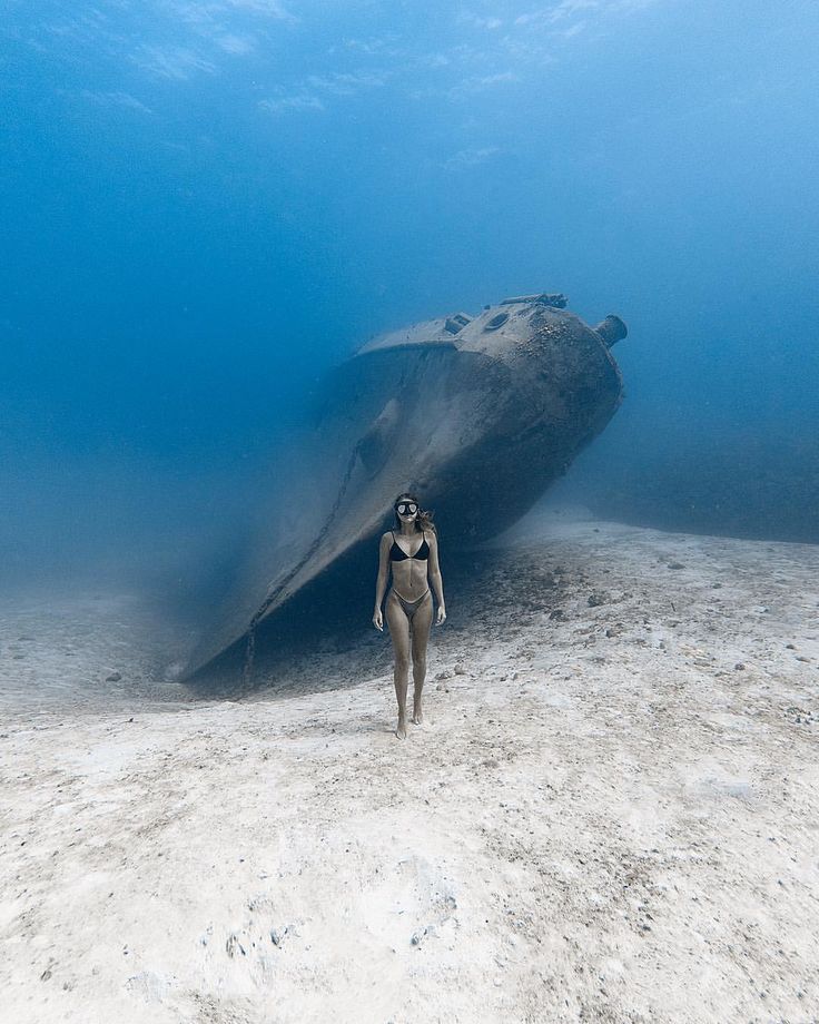 a woman in a diving suit is walking on the sand with a large object behind her