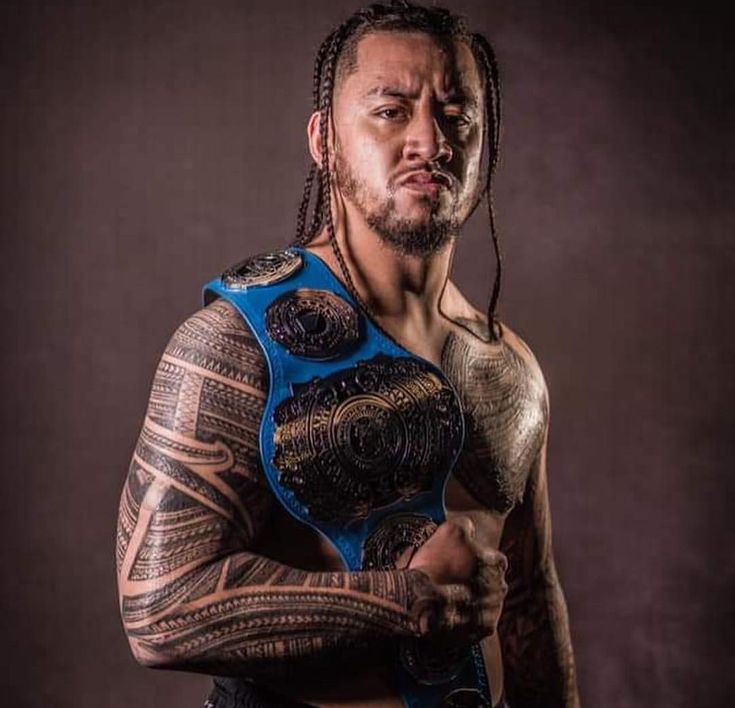 a man with tattoos on his arms and chest holding a wrestling belt in front of his face