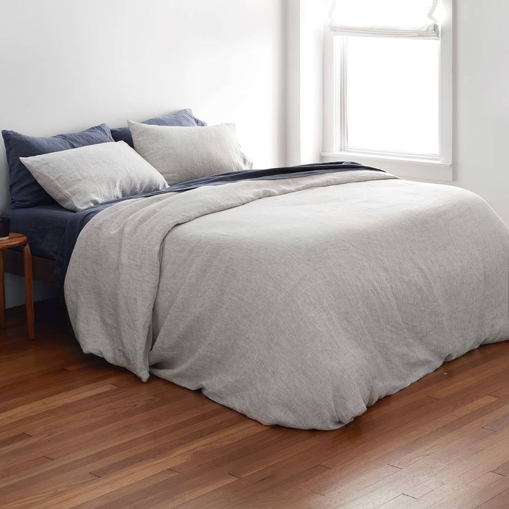 a bed sitting on top of a hard wood floor next to a window with white walls