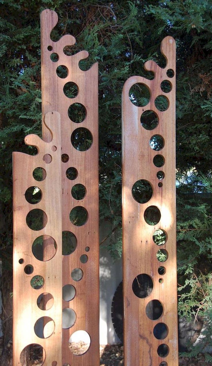 two wooden sculptures with holes in them sitting on the ground next to some bushes and trees