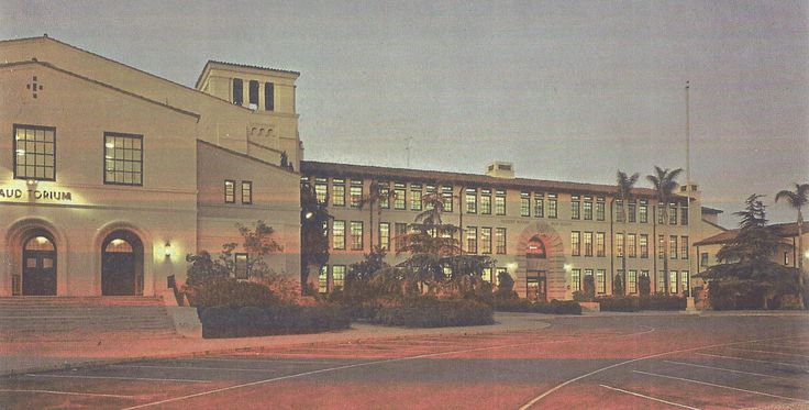 an old building with a tennis court in front of it at night, lit up by street lights