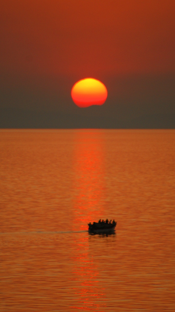 a small boat floating on top of a large body of water under a red sky