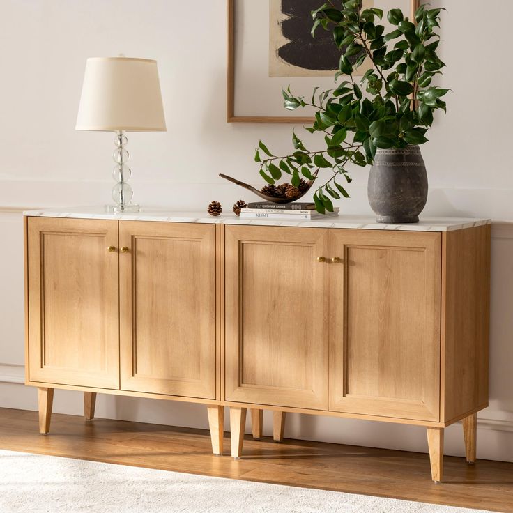 a plant is sitting on top of a wooden cabinet next to a lamp and pictures