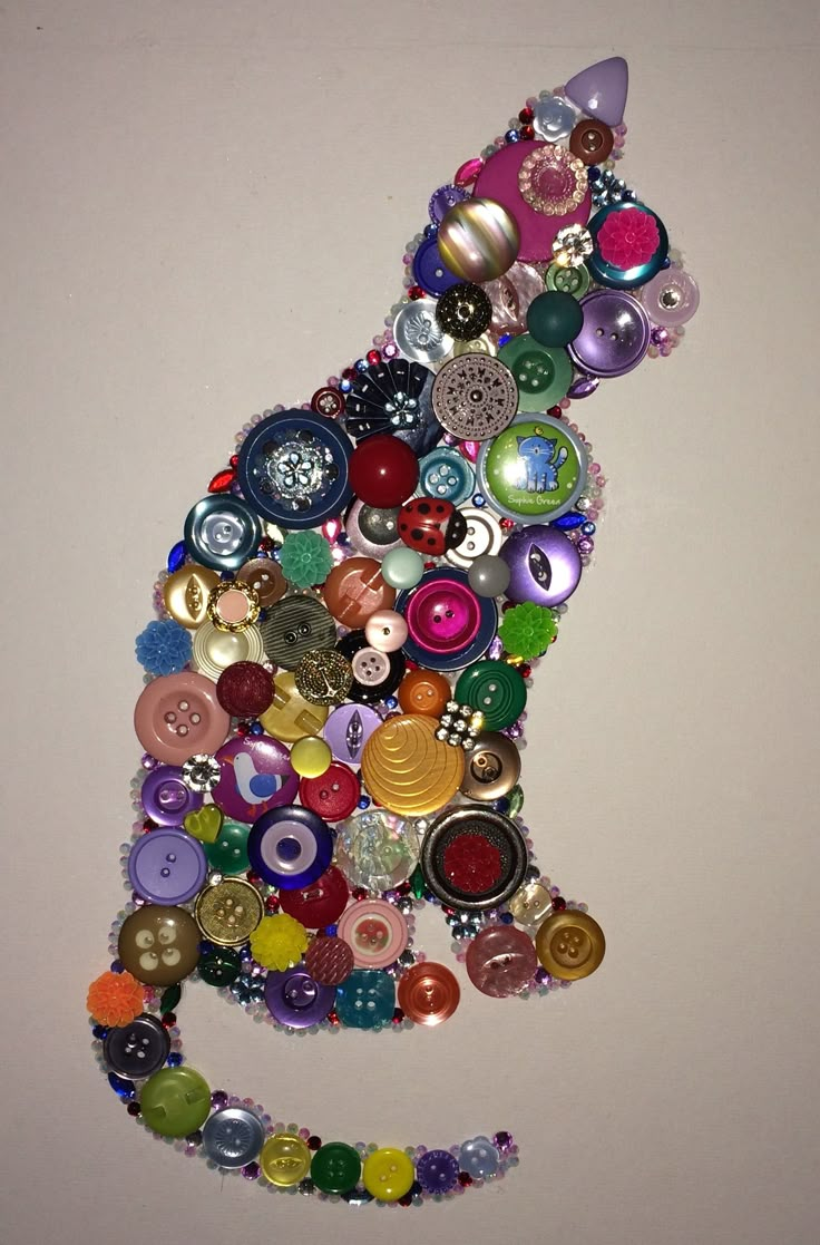 a cat made out of buttons and beads on a white wall with a gray background