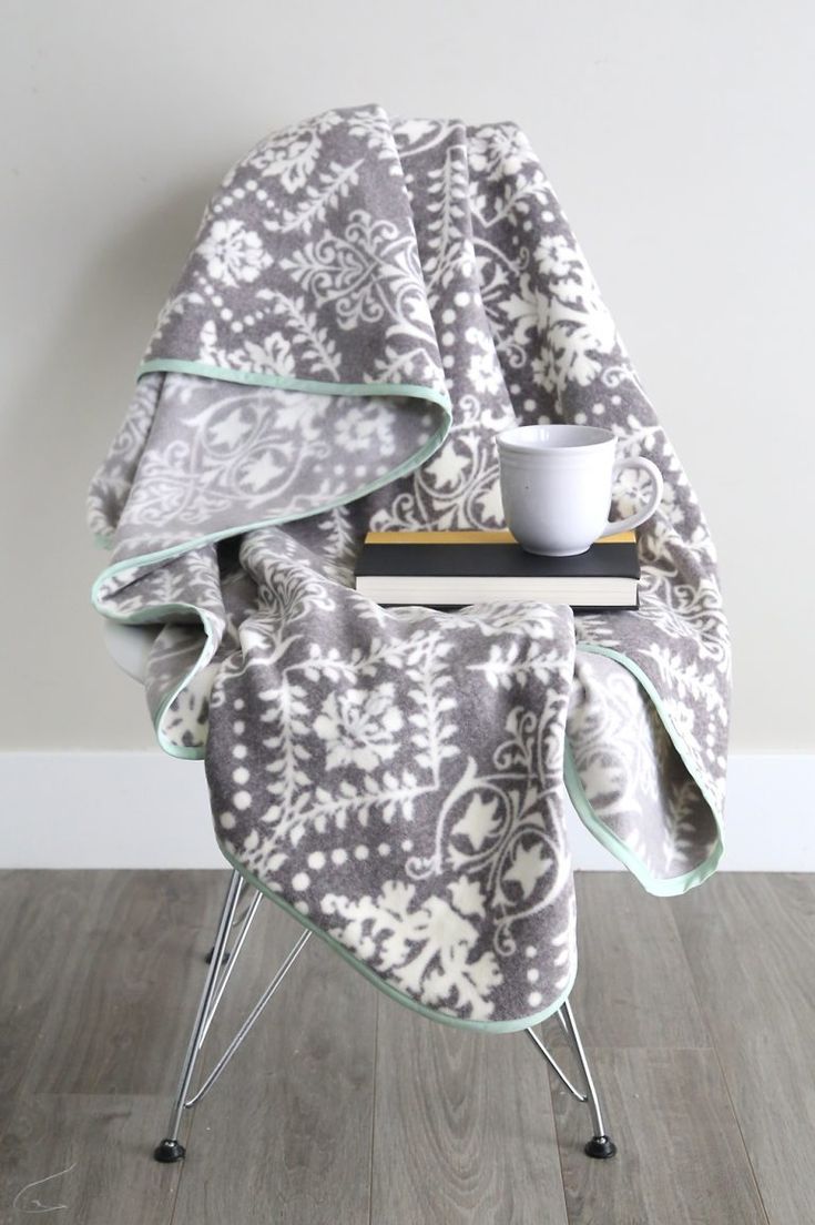 a gray and white blanket sitting on top of a chair next to a coffee cup