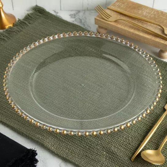 an empty plate on a green placemat with gold beaded trim and silverware