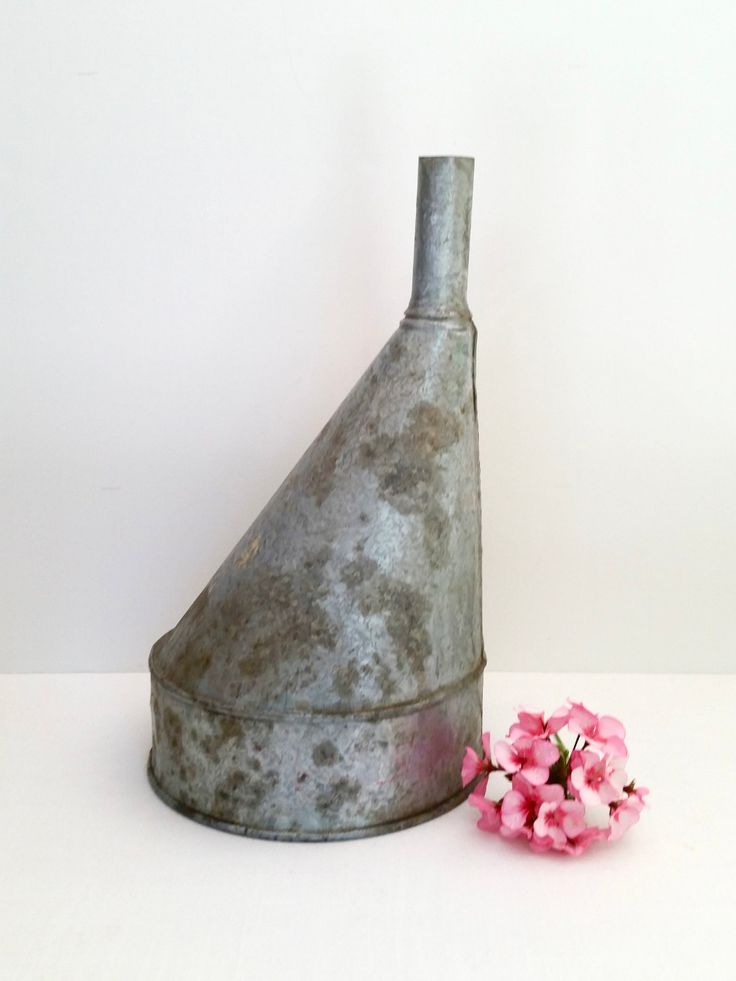 a metal vase with pink flowers in it next to a white wall and a flower pot