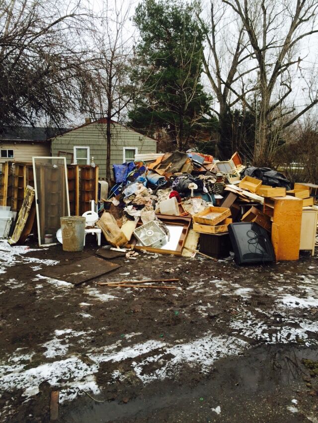 a pile of trash sitting in the middle of a yard next to a house and trees