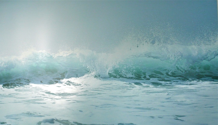 an ocean wave crashing into the shore on a cloudy day with sunbeams in the background