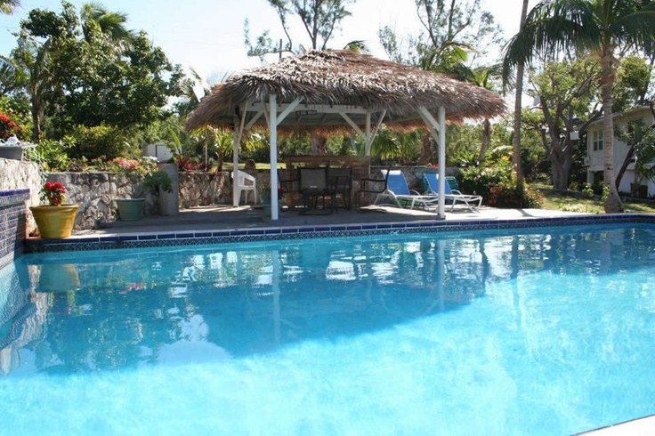 an empty swimming pool with a thatched roof and lounge chairs next to the pool