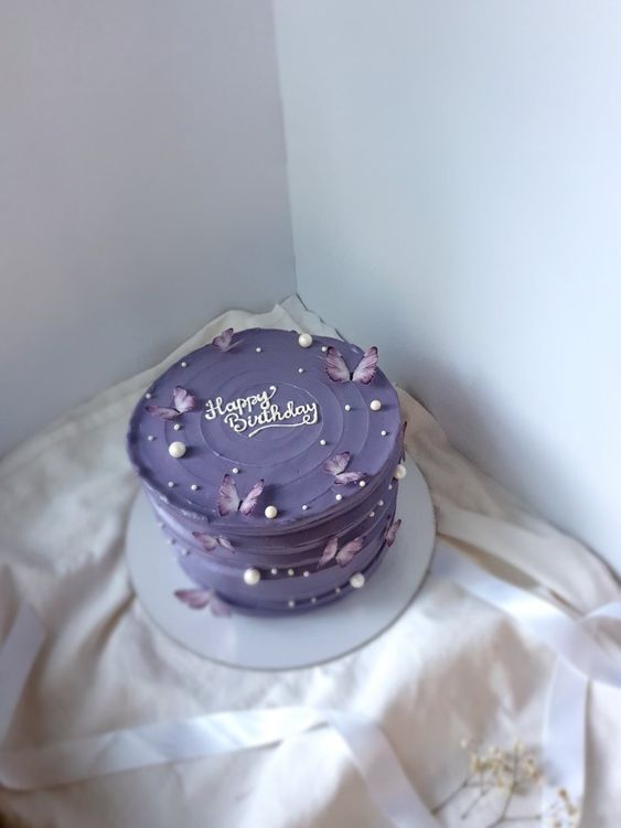 a purple birthday cake sitting on top of a white tablecloth covered floor next to a wall