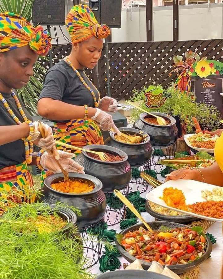 several people are serving themselves food from bowls and plates on a table with grass in front of them