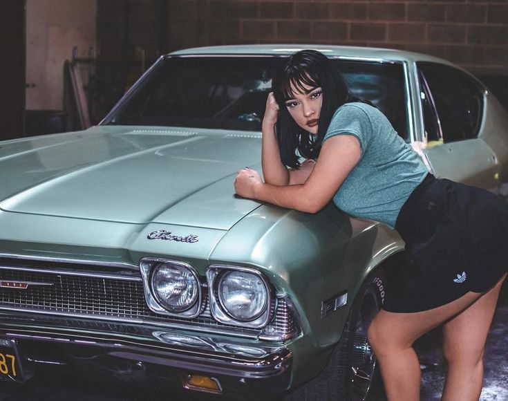 a woman leaning on the hood of a green car