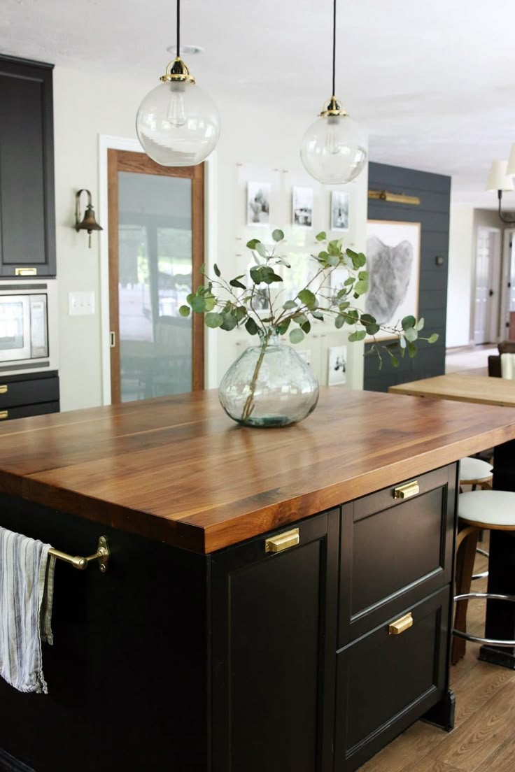 a kitchen with black cabinets and wooden counter tops, hanging lights above the island area