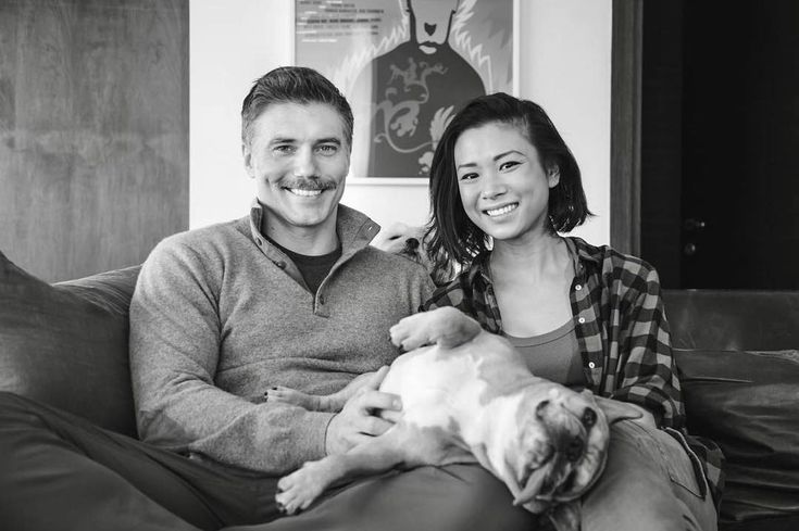 a man and woman sitting on a couch with a dog in their lap, smiling at ...