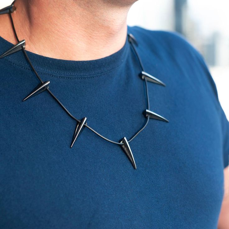 a man wearing a blue t - shirt and black necklace with metal spikes on it