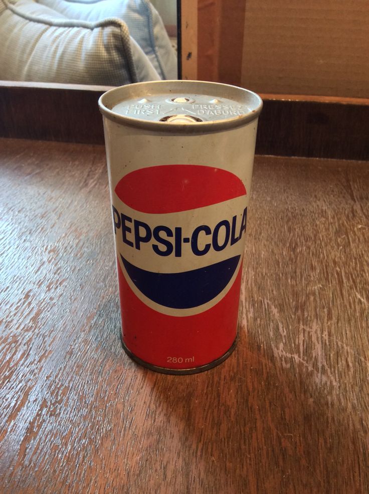 a can of pepsi cola sitting on top of a wooden table next to a bed