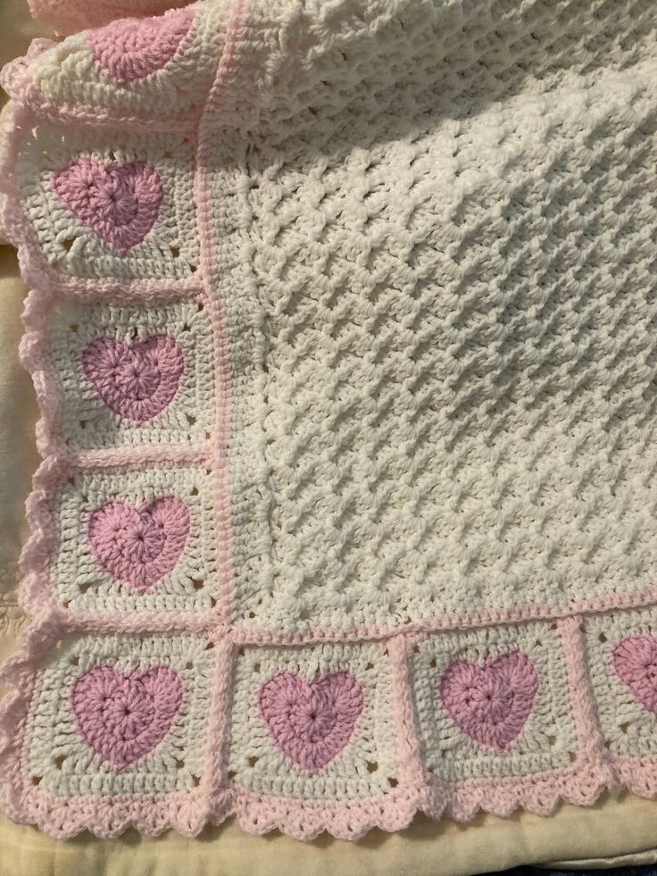 a crocheted blanket with pink hearts on it and a white pillow next to it