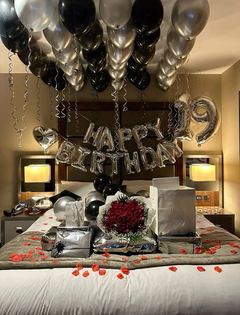 a bed topped with lots of silver and black balloons next to a sign that says happy birthday