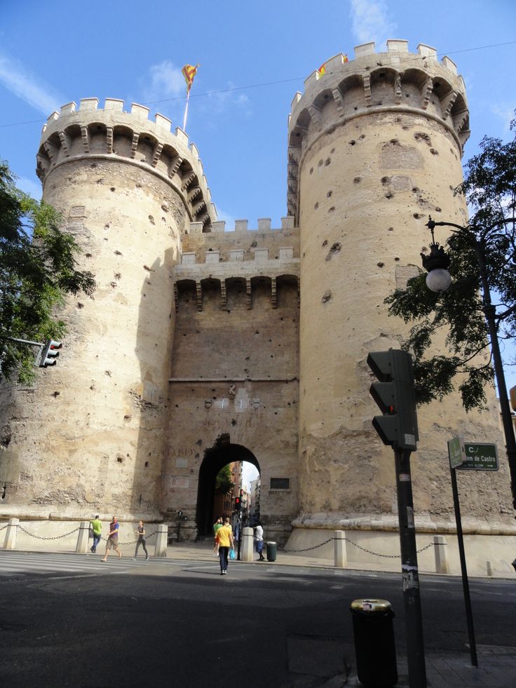 people are walking in front of an old stone castle with a gate on the side