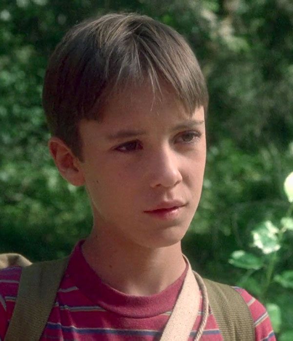 a young boy wearing a backpack and looking at the camera with trees in the background