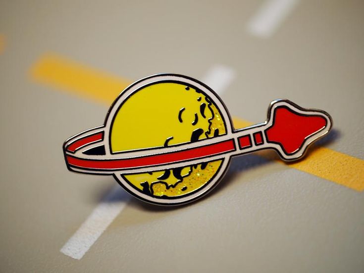 a yellow and red pin with an arrow in the shape of a planet on it