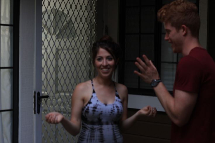 a man standing next to a woman in front of a door holding her hand out